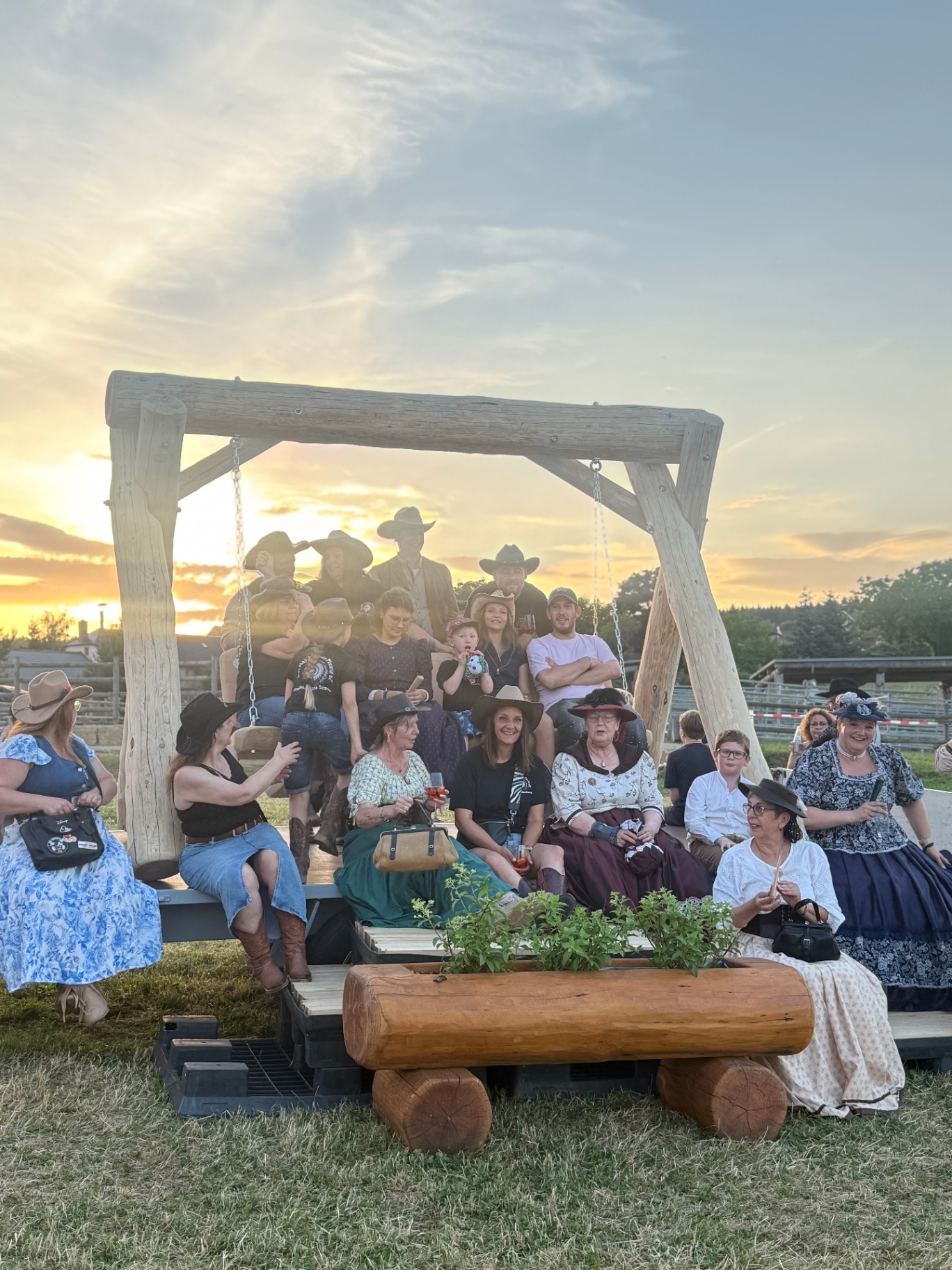 Große Familie und Freunde auf einer massiven Baumstamm-Sitzgruppe im Sonnenuntergang